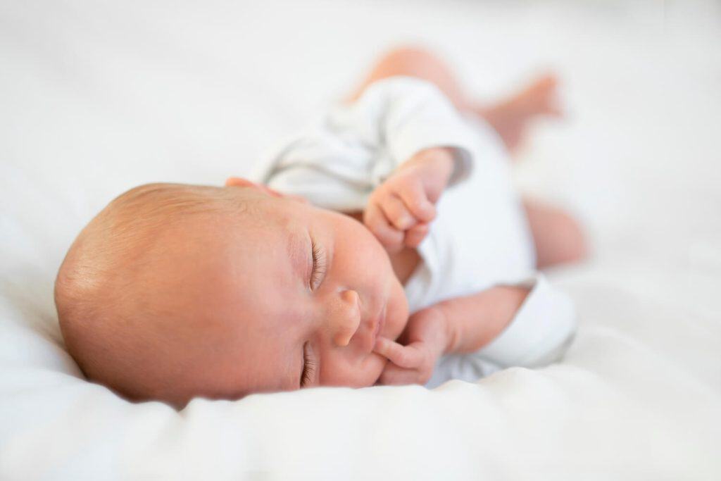 Pasgeboren baby in een wit rompertje op zijn zij op een witte deken