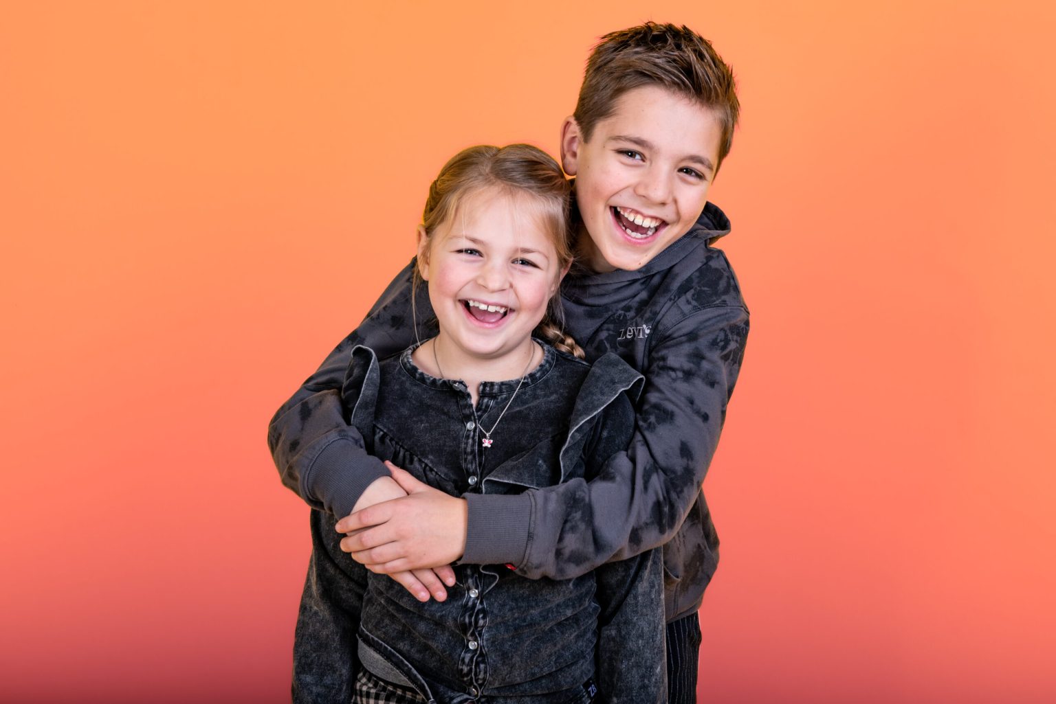 Broer en zus lachen samen tegen een perzikkleurige achtergrond in de studio