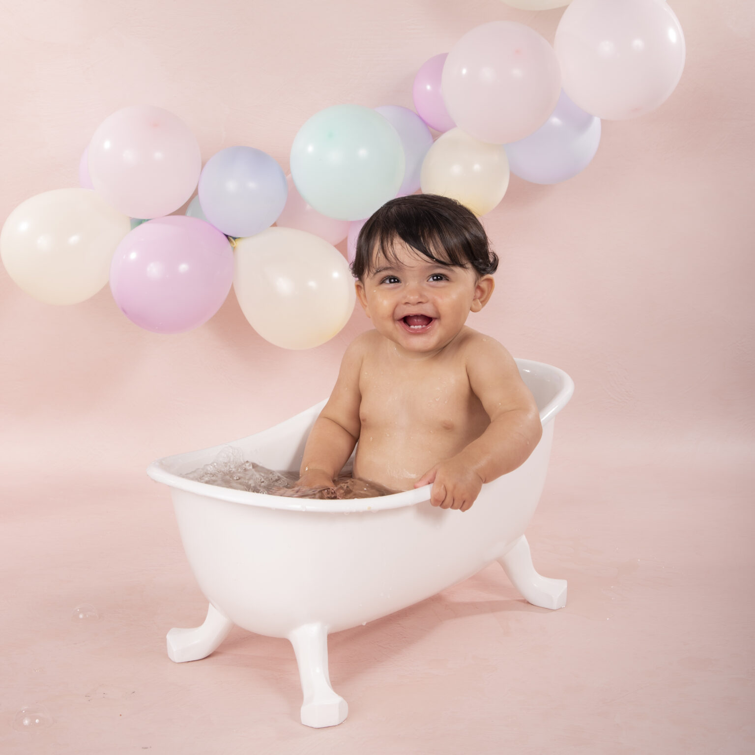 Lachende baby in een wit badje bij een pastelkleurige ballonnenboog