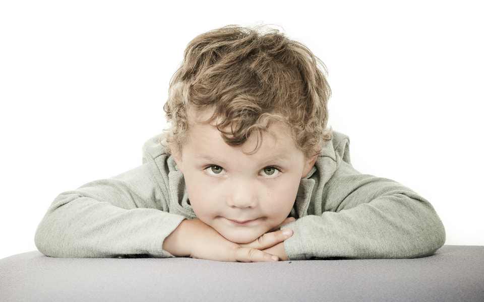 Jongen leunt met zijn kin op zijn handen tegen een groene achtergrond