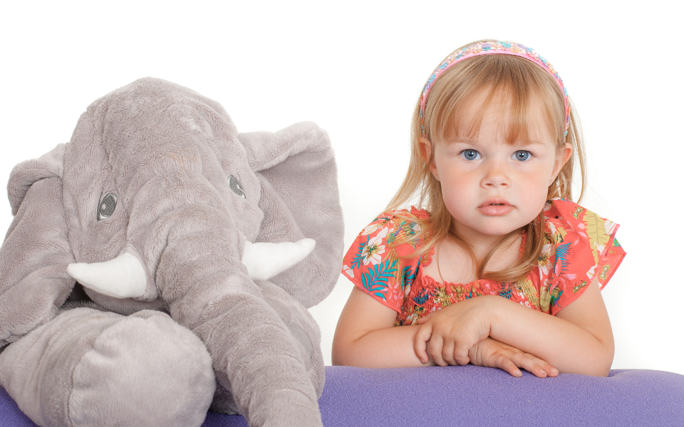 Peuter naast een grote knuffelolifant op een witte achtergrond