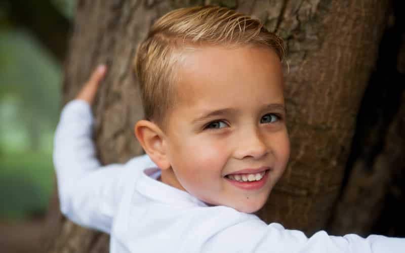 Jongen leunt lachend tegen een boom tijdens een fotoshoot buiten
