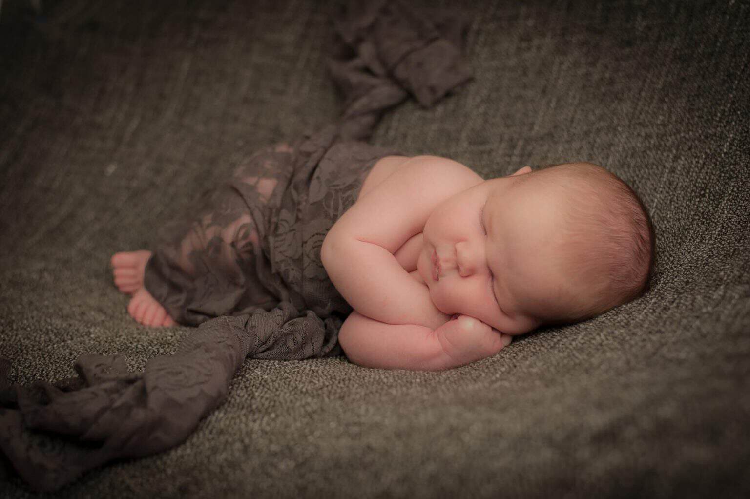 Pasgeboren baby opgekruld in een bruine wrap op een donkere ondergrond
