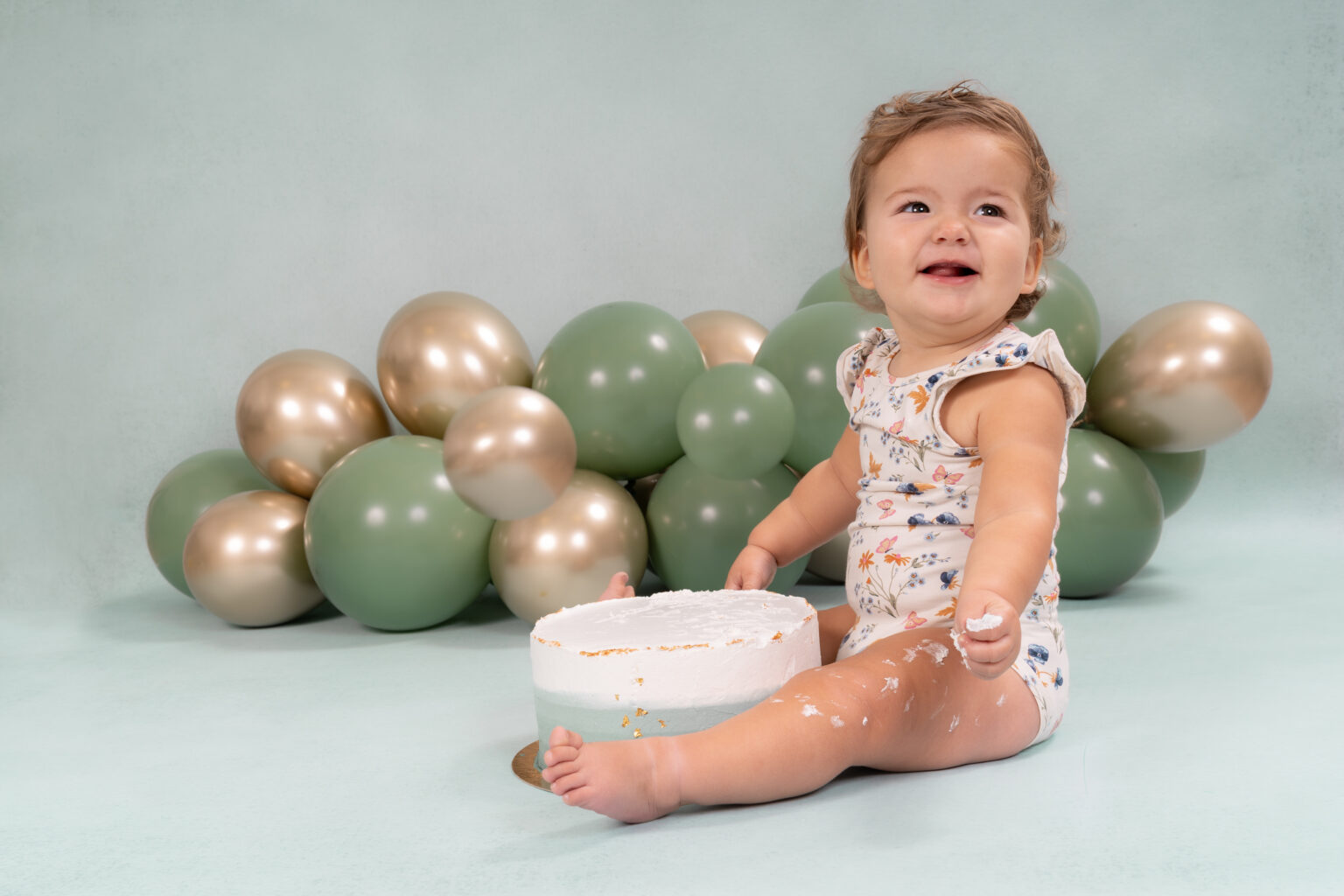 Lachend meisje bij groene en gouden ballonnen tijdens een cakesmash fotoshoot
