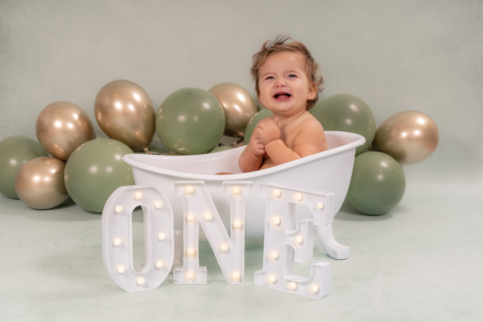 Jongetje in een wit badje bij groene en gouden ballonnen met ONE letters