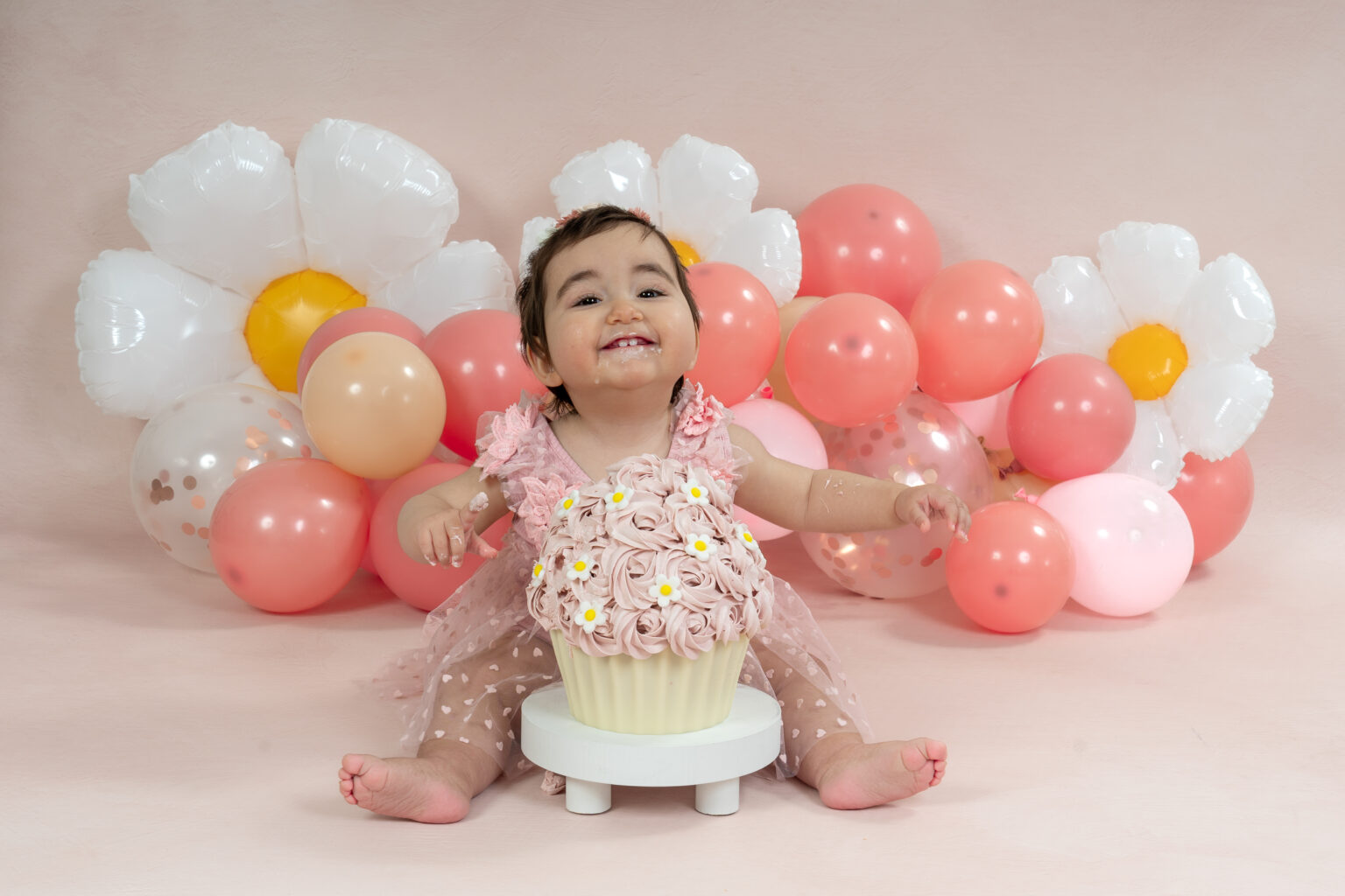 Meisje in roze jurk met een cupcake bij witte madeliefjes ballonnen