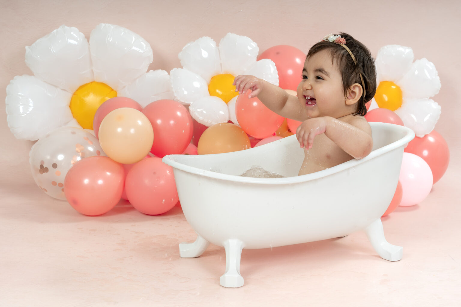 Meisje in een wit badje bij witte madeliefjes ballonnen in roze en perzik