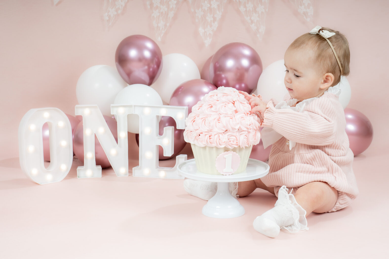 Meisje in roze jurk kijkt naar haar cakesmash taart bij de ONE letters