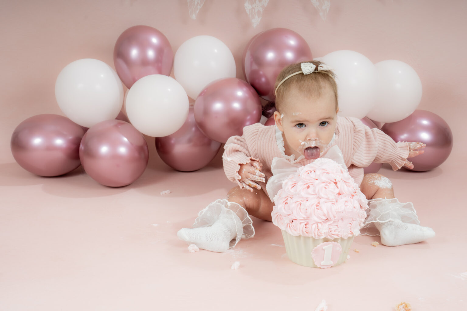 Meisje in het roze bij roze en witte ballonnen met haar eerste taart