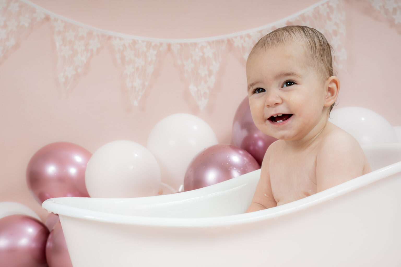 Lachend meisje in een wit badje bij roze en witte ballonnen