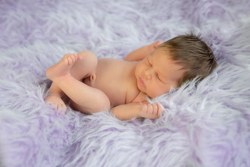 Pasgeboren baby slaapt opgekruld op een lila vacht