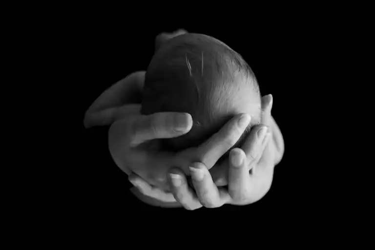 Hoofdje van een pasgeboren baby in de handen van haar ouders, in zwart wit