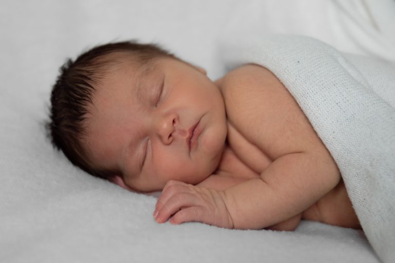 Slapende pasgeboren baby met donker haar onder een witte doek