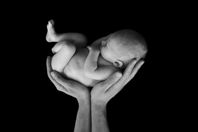 Pasgeboren baby in zwart wit, gedragen in de handen van haar ouders