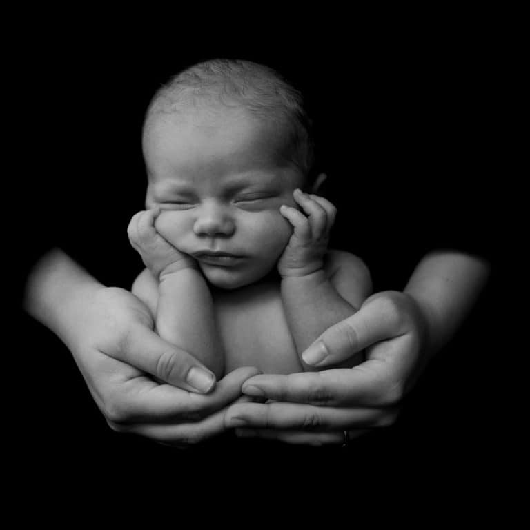 Pasgeboren baby met de handjes onder het kinnetje op een zwarte achtergrond
