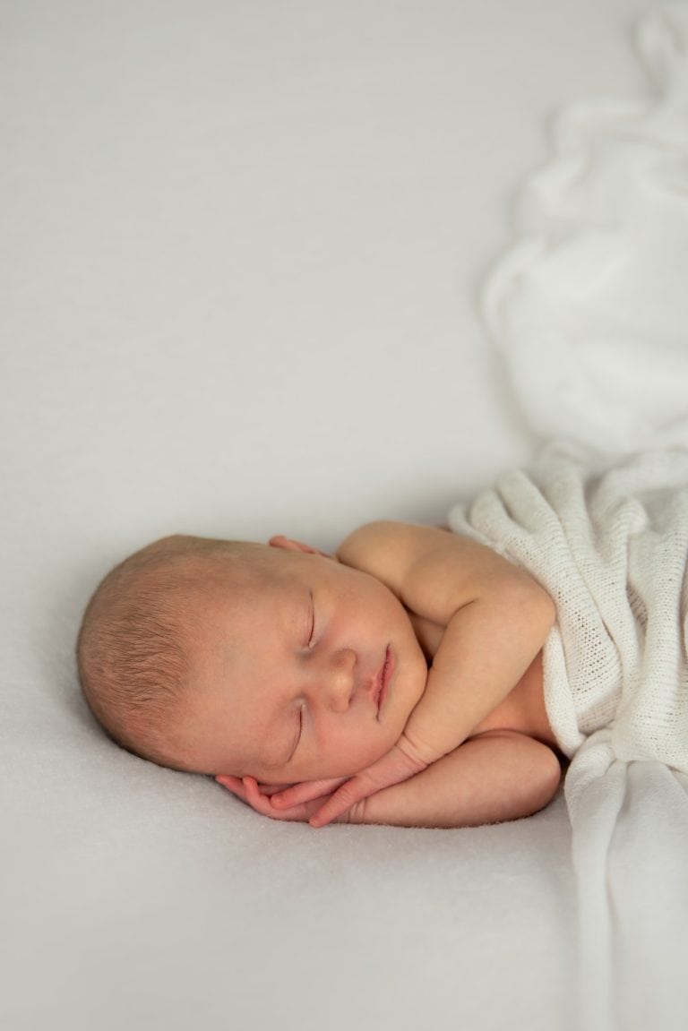 Pasgeboren baby slaapt ingebakerd op een witte deken in de studio