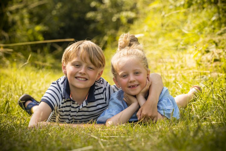 Twee kinderen liggen samen in het gras tijdens een fotoshoot op buitenlocatie