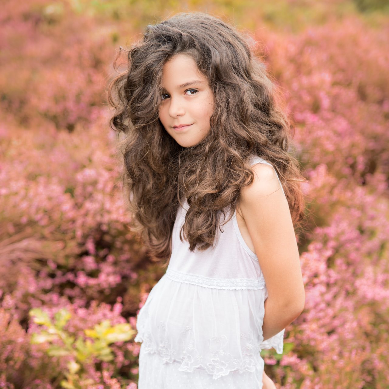 Meisje met lange krullen tussen roze bloemen tijdens een fotoshoot buiten