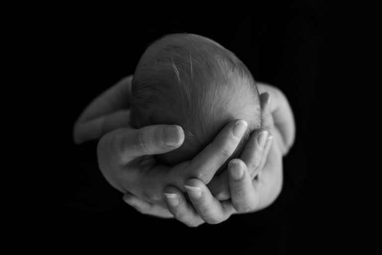 Handen die het hoofdje van een pasgeboren baby omvatten, zwart-wit