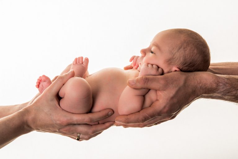 Pasgeboren baby vastgehouden door de handen van beide ouders