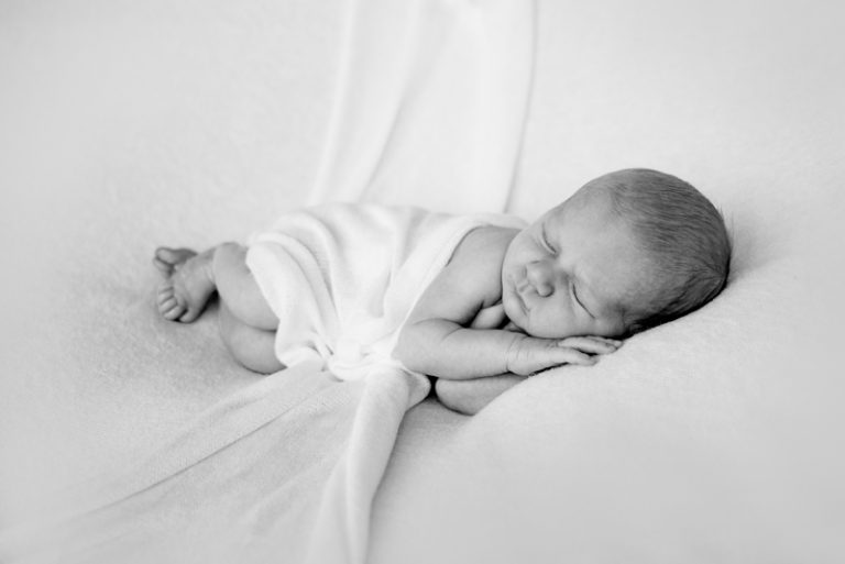 Pasgeboren baby slaapt ingebakerd op een witte deken, zwart-wit