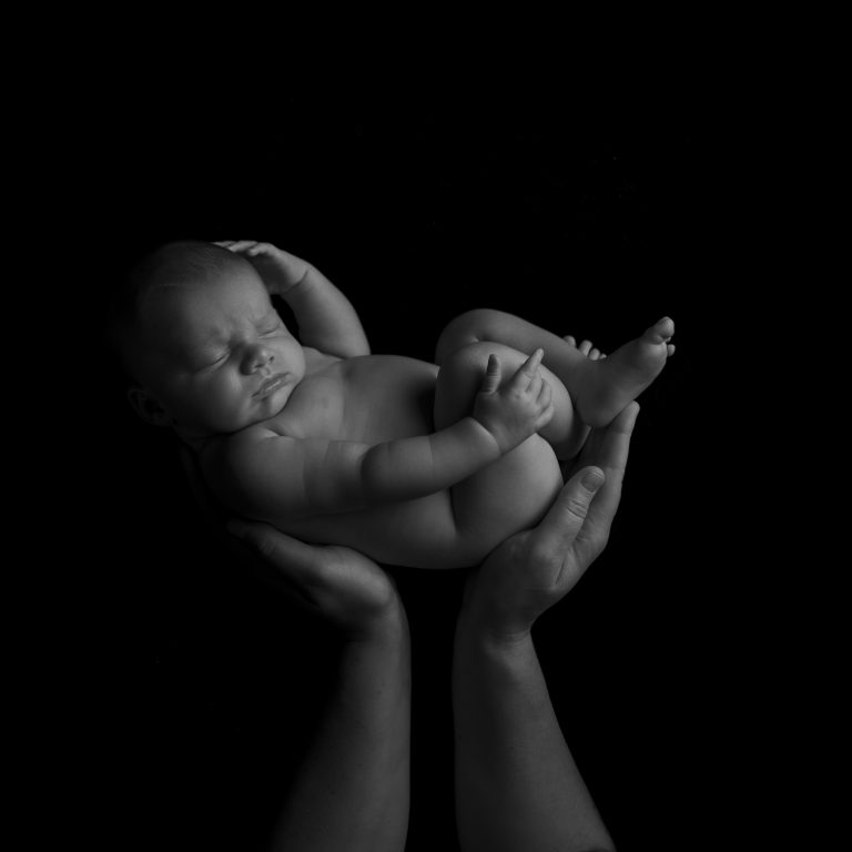 Pasgeboren baby op een zwarte achtergrond in de handen van een ouder