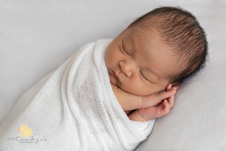 Pasgeboren baby met veel donker haar, ingebakerd in een witte doek