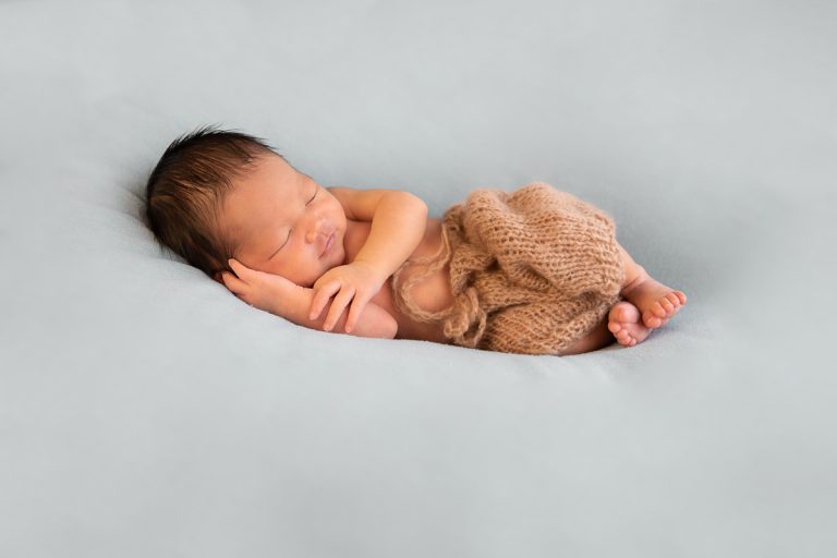 Pasgeboren baby op haar buik in een gebreid pakje tijdens een newborn fotoshoot