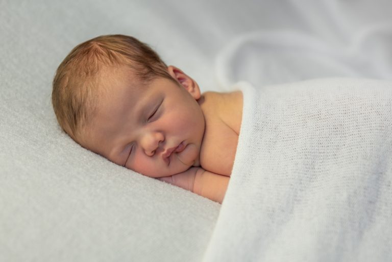 Slapende pasgeboren baby onder een zachte witte deken thuis