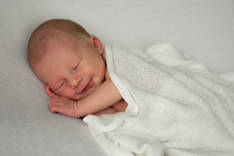Pasgeboren baby lacht in haar slaap onder een wit gebreid dekentje