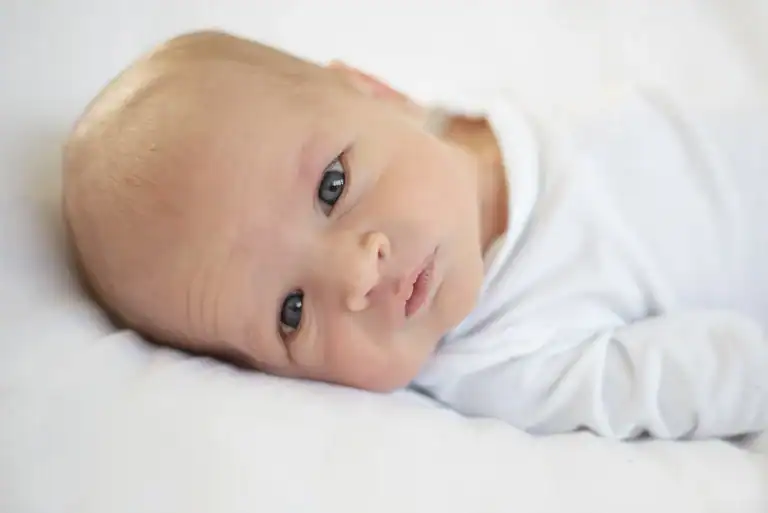 Pasgeboren baby kijkt wakker in de camera tijdens een newborn shoot aan huis