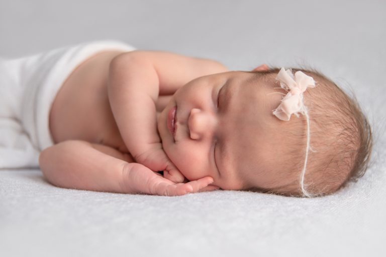 Close-up van een slapende pasgeboren baby met een wit strikje