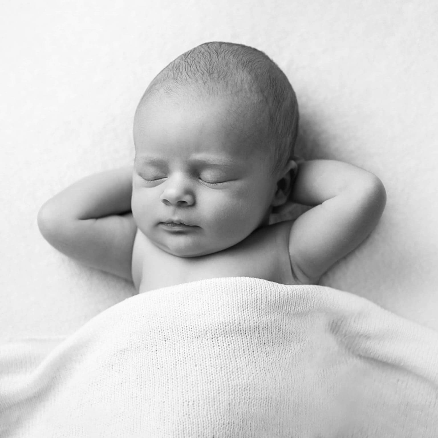 Pasgeboren baby met de handjes achter het hoofd, in zwart-wit