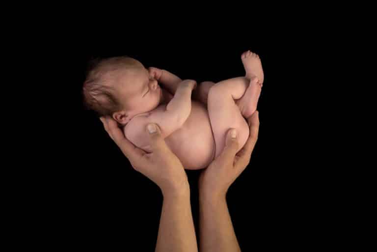 Pasgeboren baby opgekruld in de handen van haar vader tegen een zwarte achtergrond
