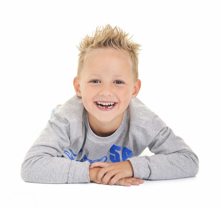 Jongen in een grijze trui lacht breed op een witte achtergrond