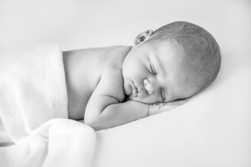 Ingebakerde pasgeboren baby die op zijn zij slaapt, in zwart-wit